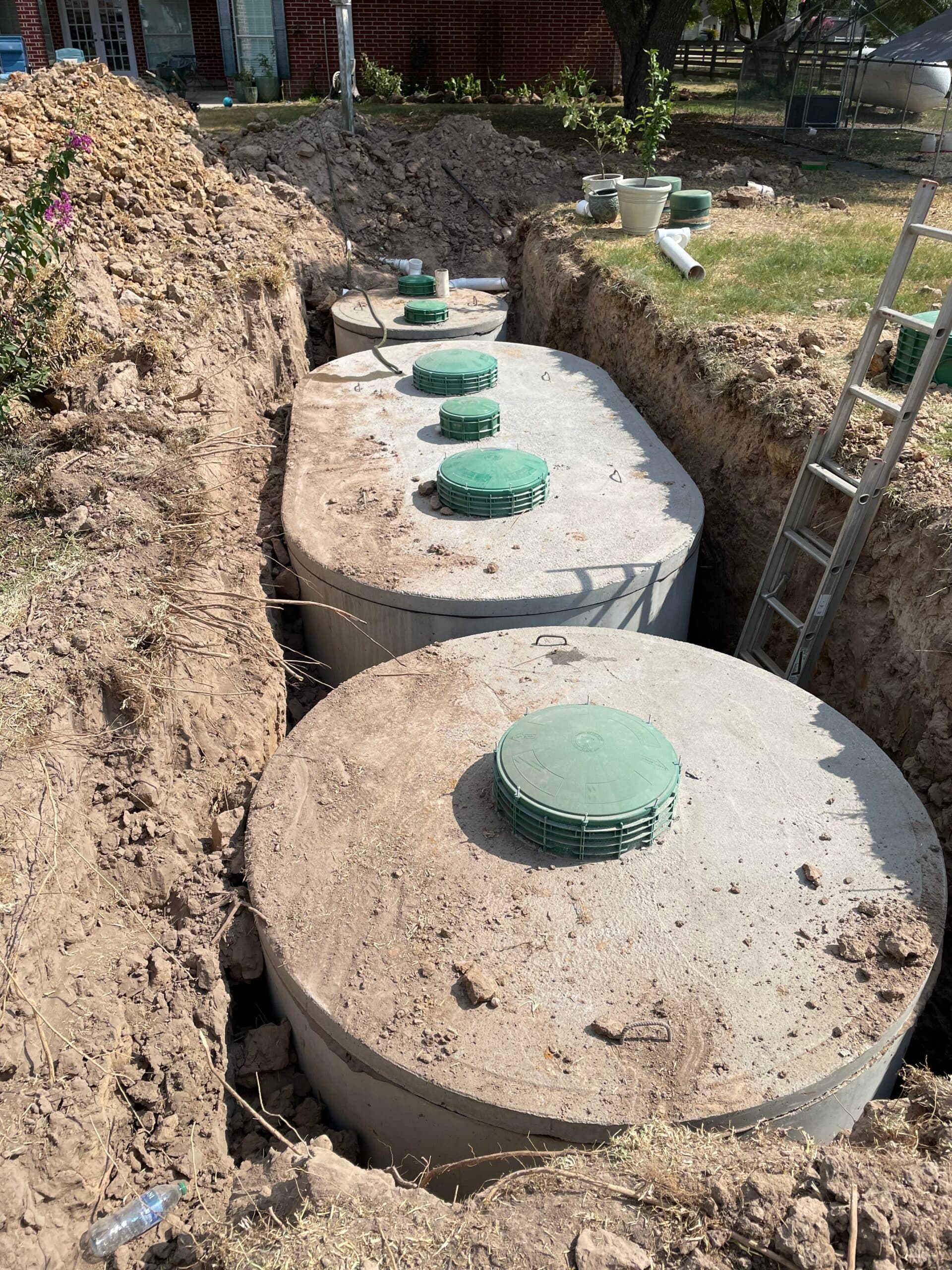 Septic tanks with green risers installed alongside a residential home